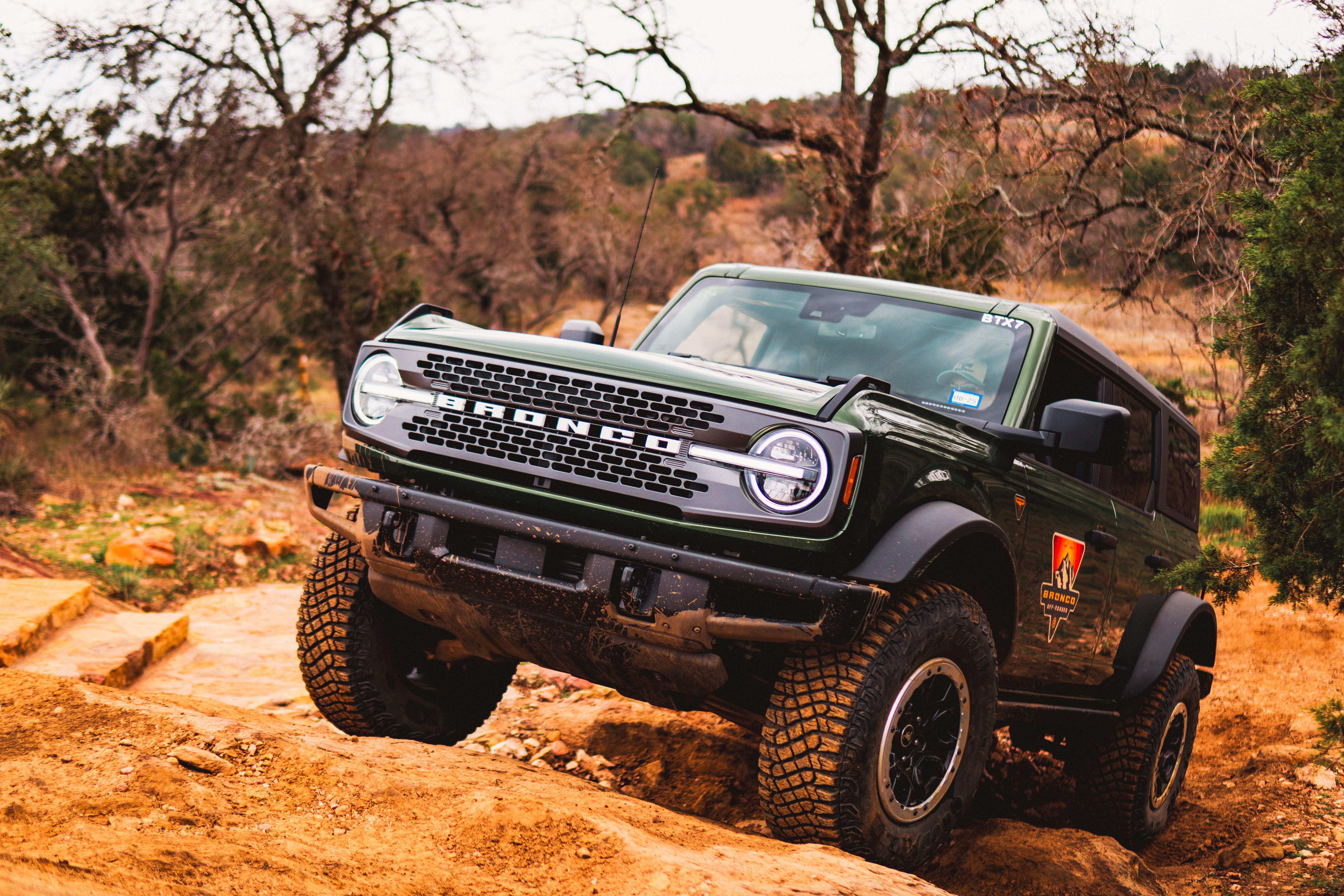 A green Ford Bronco climbs over red rocks
